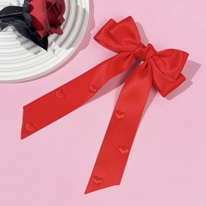 Détail d'un nœud à cheveux en satin rouge avec cœurs 3D et longs rubans sur fond rose