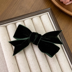 Detailed view of dark green velvet bow hair clip on a premium beige display tray