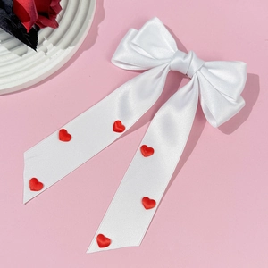 Détail d'un nœud papillon en satin blanc avec des broderies de cœurs rouges sur rubans