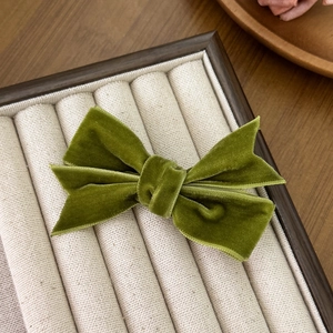 Detailed close-up of an olive green velvet bow hair clip on a beige jewelry display tray