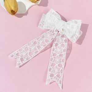 Detail of elegant white lace bow hair clip with floral patterns and long ribbons