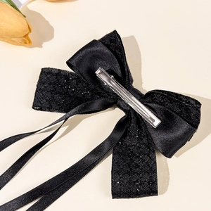 Elegant black satin bow hair clip with lace and streamers on a beige textured background