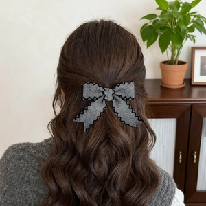 Elegant grey tweed bow hair clip with black wavy edge stitching shown on wavy brown hair