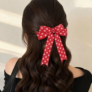 Barrette à nœud rouge avec motifs de cœurs blancs sur de longs cheveux bouclés