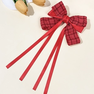 Detail of red tweed bow hair clip with long satin ribbons on elegant beige background