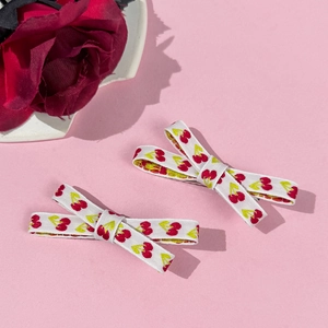 Dettaglio di fermagli per capelli con ciliegie ricamate su sfondo rosa con una rosa