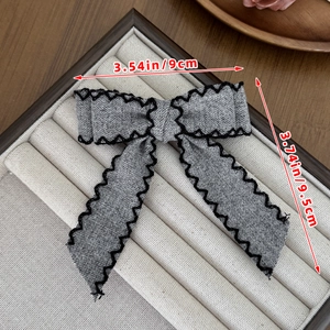Detailed view of grey bow hair clip with black wavy embroidery and size dimensions