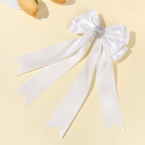 Close-up of white satin bow hair clip with sparkling rhinestone pendant and long ribbons