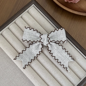 Close-up of elegant fabric bow hair clip with brown scalloped stitching on velvet tray