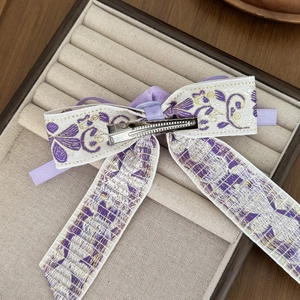 Elegant Chinese style purple floral embroidered bow hair clip on a beige jewelry display