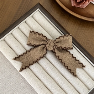 Close-up of a brown bow hair clip with wavy edges and stitching detail on soft velvet box