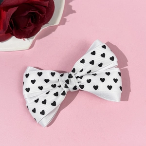 Détail de la barrette nœud blanc avec motifs cœurs sur une surface rose poudré