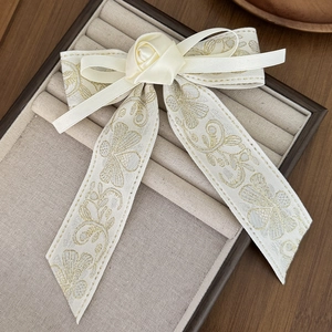 Close-up of cream bow hair clip with silk rose and gold floral embroidery pattern