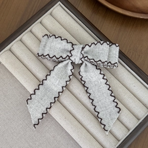Close-up of double-layer bow hair clip with brown scalloped edges on velvet tray