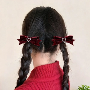 Détail de barrettes nœuds en velours bordeaux avec strass en cœur sur cheveux tressés