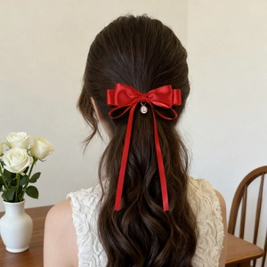 Red satin bow hair clip with white pearl pendant shown on a model's half-up hairstyle