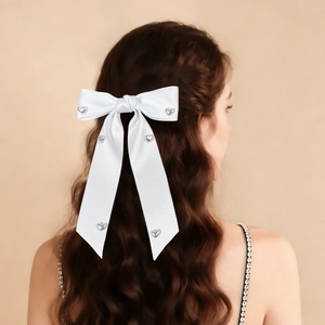 Detailed back view of a white satin bow hair clip with silver heart studs on wavy brown hair