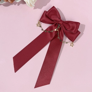 Close-up of a burgundy satin bow hair clip with gold star chains and long streamers