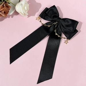 Detail of black satin bow hair clip with golden star chain and elegant long ribbon streamers