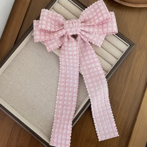 Barrette à nœud à carreaux roses avec de longs rubans sur un plateau à bijoux beige