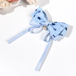 Détail de la barrette nœud en satin bleu clair avec motifs de cœurs et perle blanche