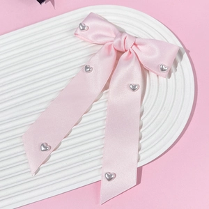 Detail of pink satin bow hair clip with silver heart buckles and long ribbons on a white tray