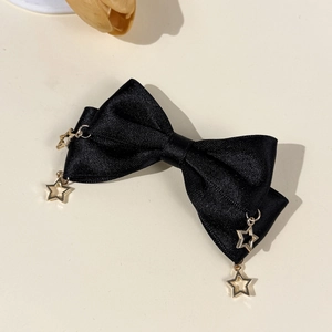 Detail of black satin bow hair clip featuring dangling golden star charms on creamy background