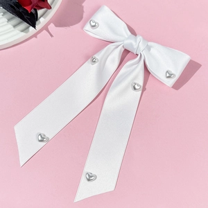 Close-up of white satin bow hair clip with silver heart studs and ribbon streamers