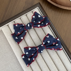 Détails de pinces à cheveux avec nœud bleu marine, motifs cœurs et bordure rouge