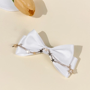 Close-up of white satin bow hair clip with gold star chain charms on a soft beige background