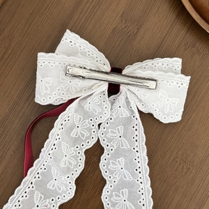 Elegante fermaglio per capelli in pizzo bianco con nastro rosso scuro su legno