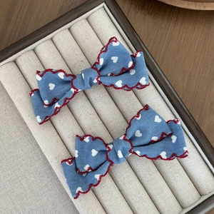 Détail de barrettes nœuds bleu clair avec motifs cœurs et bordure brodée rouge ondulée