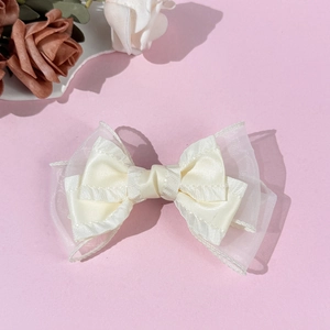 Dettaglio del fermaglio per capelli a doppio fiocco in mesh crema su sfondo rosa elegante