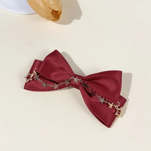 Detailed shot of burgundy satin bow hair clip with gold star chain and silk texture finish