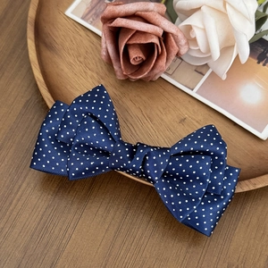 Detail of multi-layered navy blue polka dot satin bow hair clip on a wooden tray