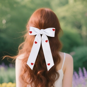 Detail of red heart bow hair clip with long ribbons worn on red wavy hair