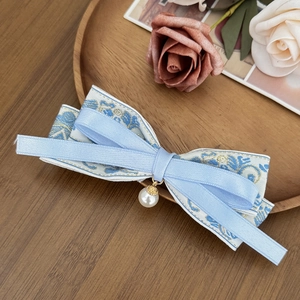 Detailed macro of light blue bow hair clip with floral embroidery and pearl pendant