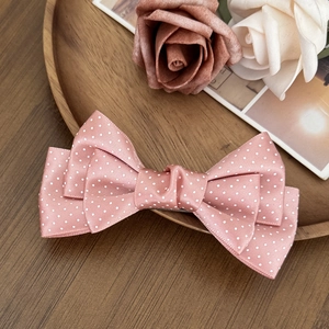 Sweet pink polka dot bow hair clip for girls with a satin finish on a wooden tray