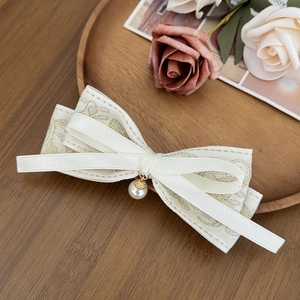 Detail of cream bow hair clip with gold floral embroidery and dangling pearl pendant