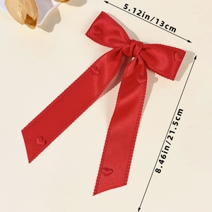 Detail showing red satin bow hair clip with heart accents, sized 13cm by 21.5cm