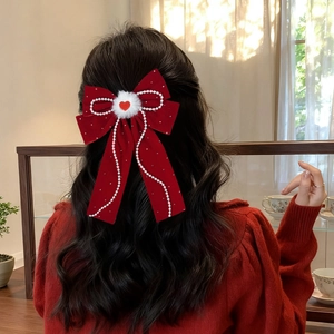 Detail of red velvet bow hair clip with pearls and heart charm on a half-up hairstyle