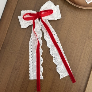 Dettaglio di un fermaglio per capelli in pizzo bianco con fiocco di velluto rosso e nastri