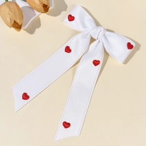 Close-up of white satin bow hair clip with red hearts and jagged edges on beige background