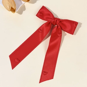Detail of red satin bow hair clip with embossed hearts and jagged stitched edge trim