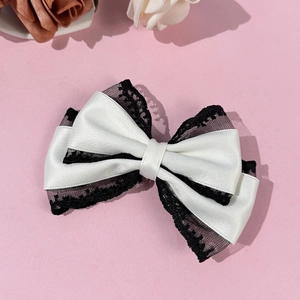 Detailed view of elegant white satin and black lace bow hair clip on pink surface
