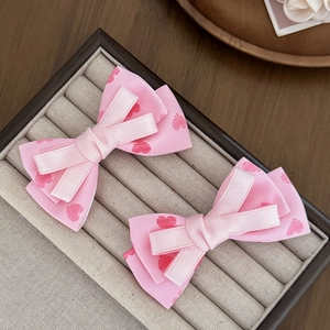 Détail de barrettes à nœuds roses avec motifs de cœurs dans un écrin à bijoux beige