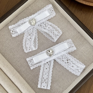 Lace bow hair clips with rhinestone hearts on a beige fabric jewelry display tray