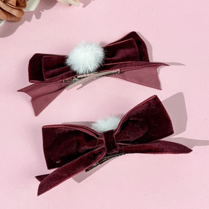 Detalle de dos pinzas para el pelo con lazos de terciopelo granate y pompones blancos