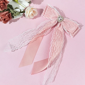 Détail du nœud en dentelle rose avec cristal en cœur, perles et longs rubans