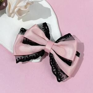 Close-up of pink satin bow hair clip with delicate black lace trim on a white plate